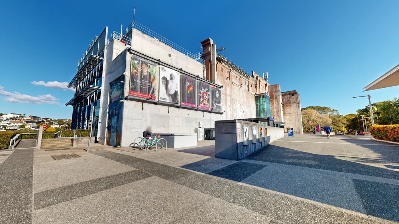 A large industrial style building with an entrance to the building with the word 'Vertigo' written above, There are blue mats at the entrance. To the left are signs advertising upcoming events.