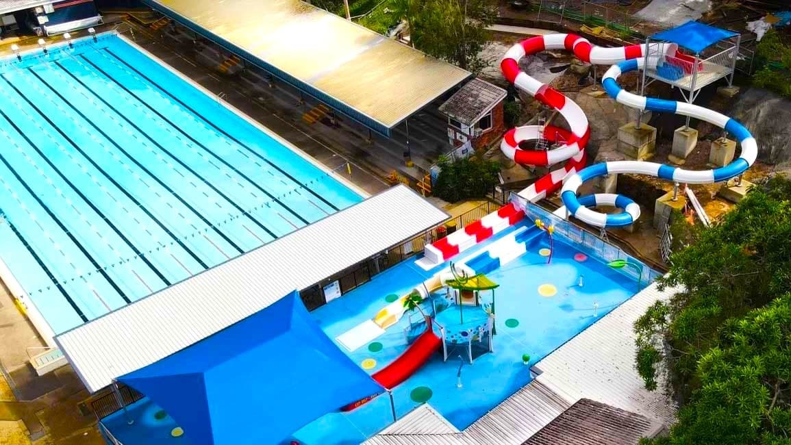 The Nambour Aquatic Centre taken from a drone approximately 100m in the air looking down onto the venue.  Most of the 50m outdoor pool is shown in the top left of the image and the splash park and flume rides to the right.