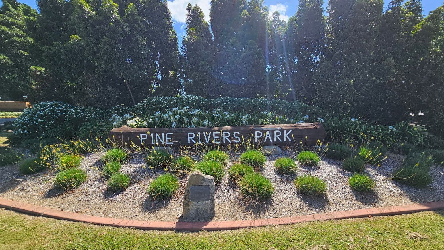 A garden featuring a range of ground cover and shrubs. A wooden sign states he words 'Pine Rivers Park'.