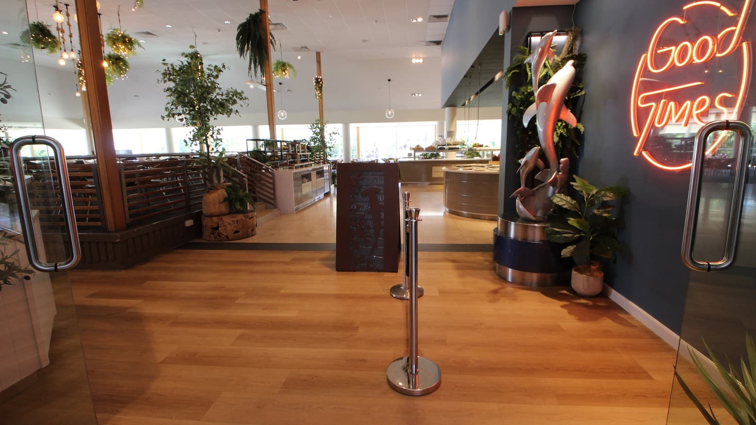 Taken directly at the entrance to The Shoreline restaurant it is possible to view the large servery and buffet benches toward the top right.  Toward the left are various seating and table options on an elevated 3 step platform.  Directly in front is a small queueing rope and dark brown flooring.