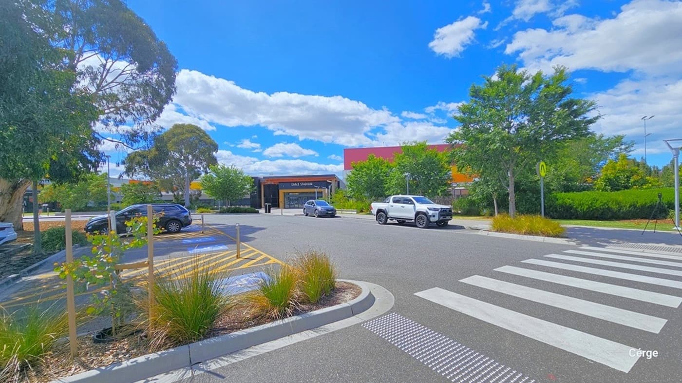 Accessible car parking spaces close to the entrance of Eagle Stadium are marked by a blue background with a white accessible logo for persons with mobility disabilities at the bottom. Between the 14 accessible car park spaces available are yellow diagonal lines enclosed by a yellow rectangle and a metal bollard. Near it is a white zebra crossing with yellow pedestrian signage represented by half-walking legs. A step-free pathway leads to the entrance doors.