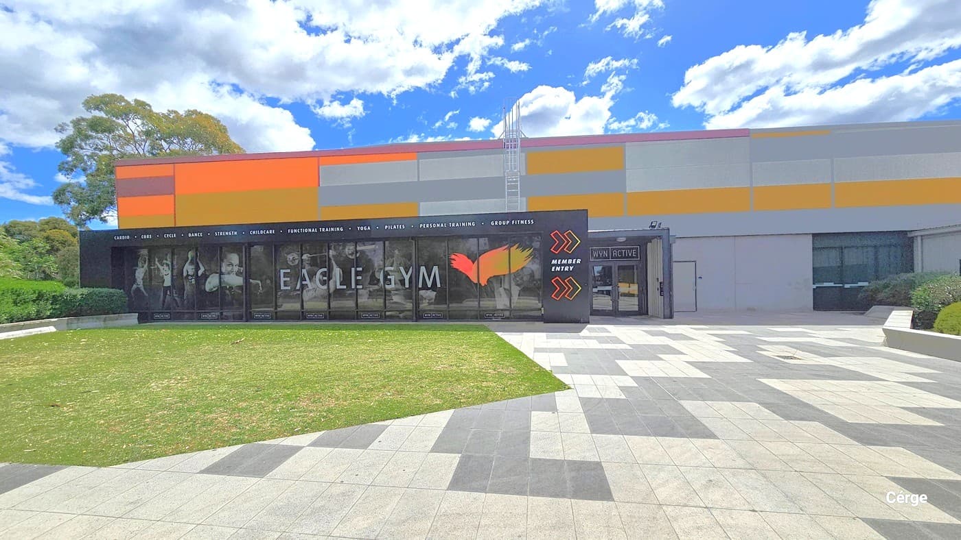 Eagle Gym entrance. The floor area outside of the gym can be differentiated by the polygon-shaped grass section and alternating light and dark grey tiles. The outside wall design of the gym is a combination of a black wall containing a white typeface listing the different gym offers and features and a glass window with an image highlighting several gym equipments as an advertisement. On the right side of the black wall is a yellow-orange outline of arrows with a white Member Entry between them.
