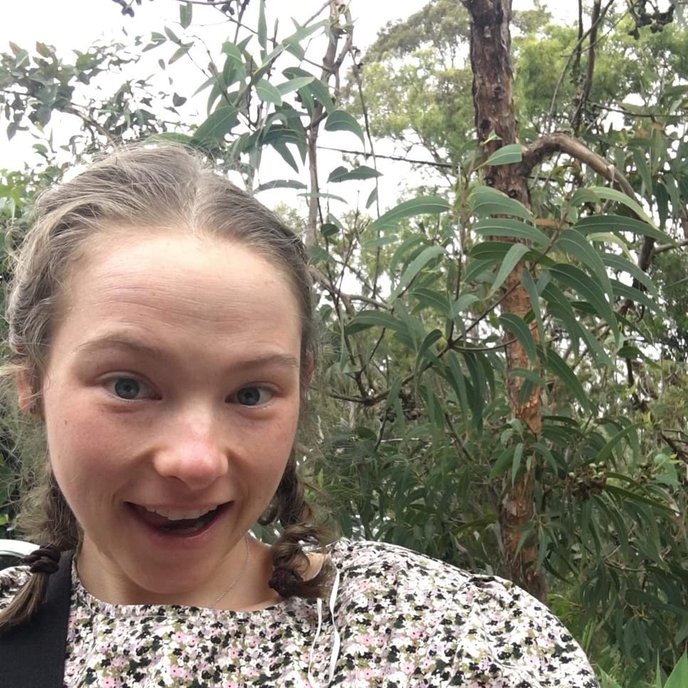 A smiling girl in a leafy outdoor setting.