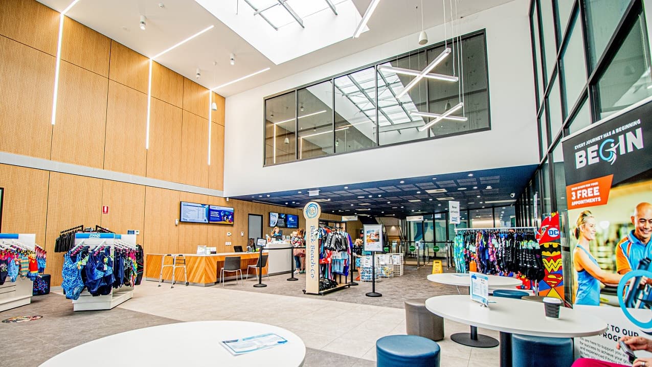 The seating area inside Gurri Wanyarra Recreational Centre has a white table supported by metal fixed strongly on the floor of the venue. Overlooking the seating table is a reception desk and a retail area.