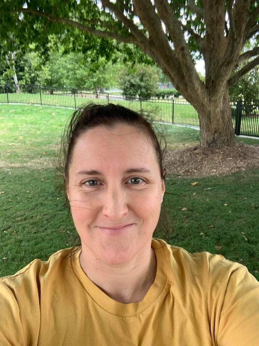 A woman with dark hair wearing a yellow shirt outdoors, smiling.