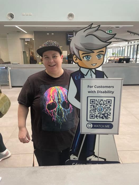 A young man with a cap posing beside a Cérge cartoon cutout with a QR sign.