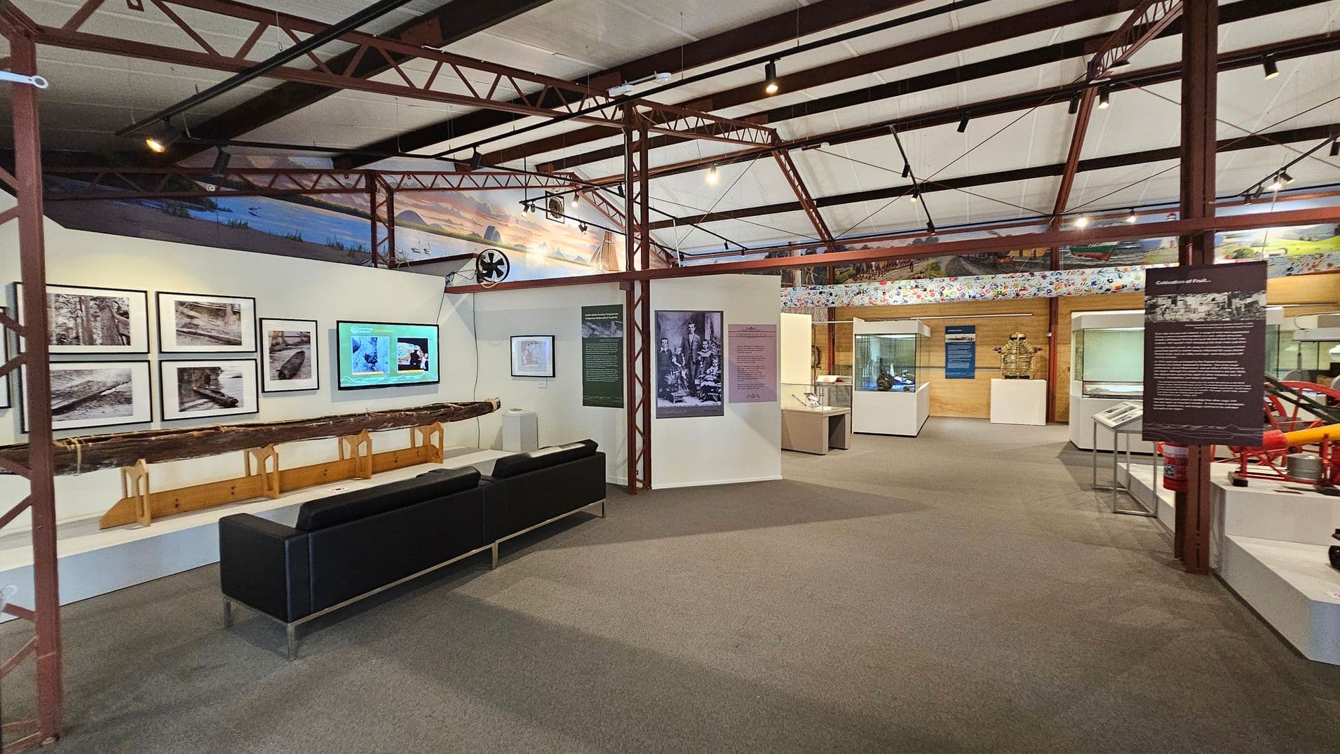 Entrance to a museum exhibit with glass doors. On the left, there are signs prohibiting eating, drinking, and touching displays. Inside, the exhibit features various displays and information panels. On the right, a panel about William Landsborough, an explorer, is visible, along with a stand holding brochures. The floor is carpeted, and the ceiling has exposed beams and lighting. Red metal pipes are visible on the left side of the entrance.