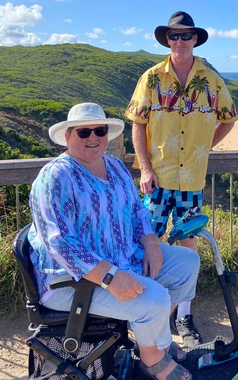 Smiling woman in a sun hat and blue patterned blouse seated outdoors.