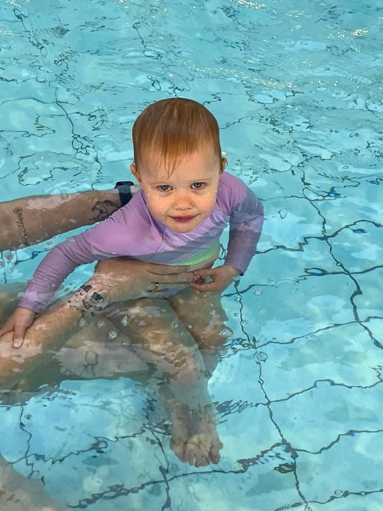 A young child in a purple swimsuit sits in a swimming pool.