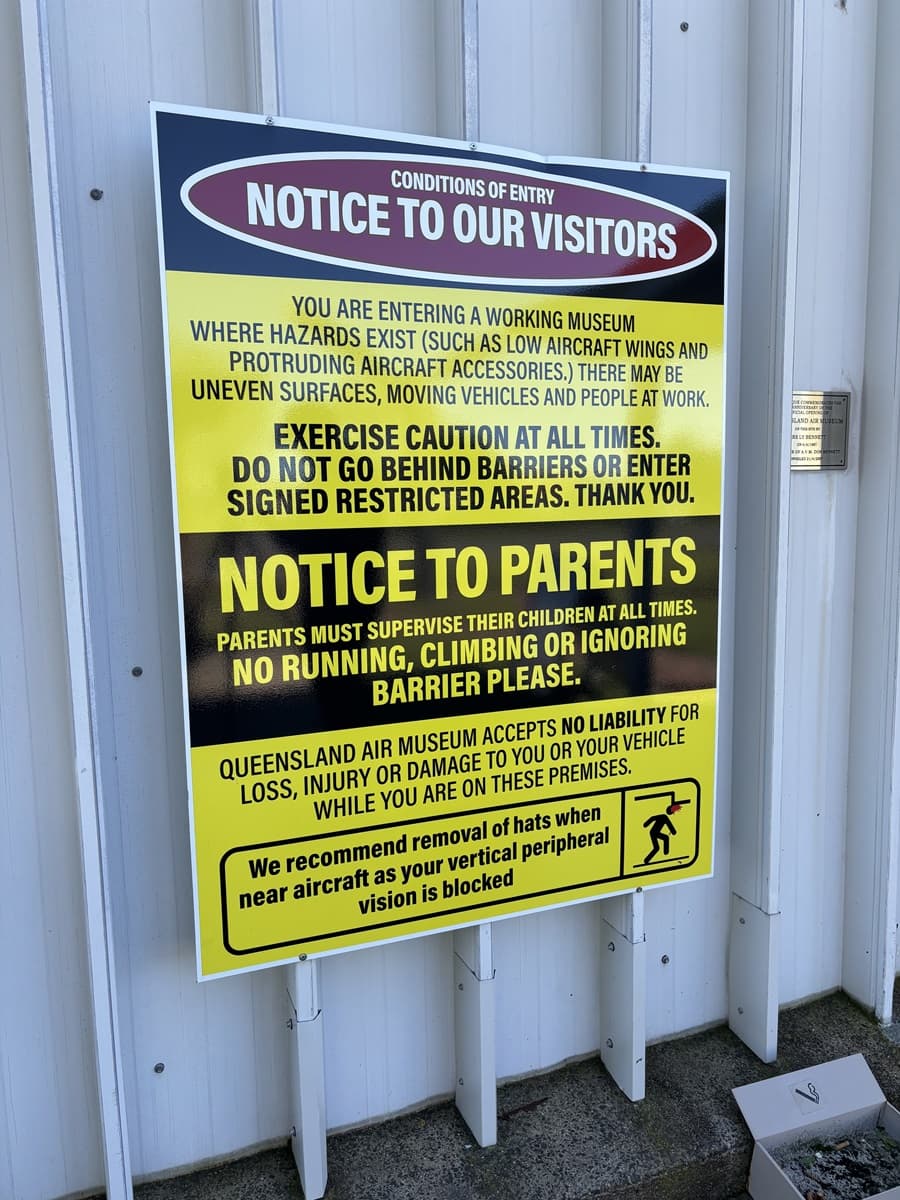 A large yellow and black sign at the entrance reads: "NOTICE TO OUR VISITORS - CONDITIONS OF ENTRY", detailing the conditions. The sign is affixed to a white metal wall with a corrugated back.