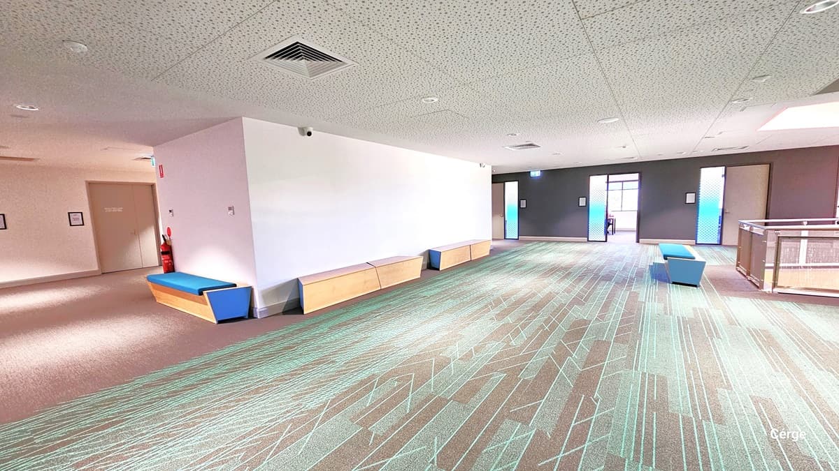 Upon entering Level One, there is a spacious area with wooden benches for seating. The floor features granite with green criss-cross line markings, and the white ceiling has fluorescent bulbs and central air conditioning. To the right, there are three partially open doors, and on the left, a fire extinguisher is mounted on the white wall.