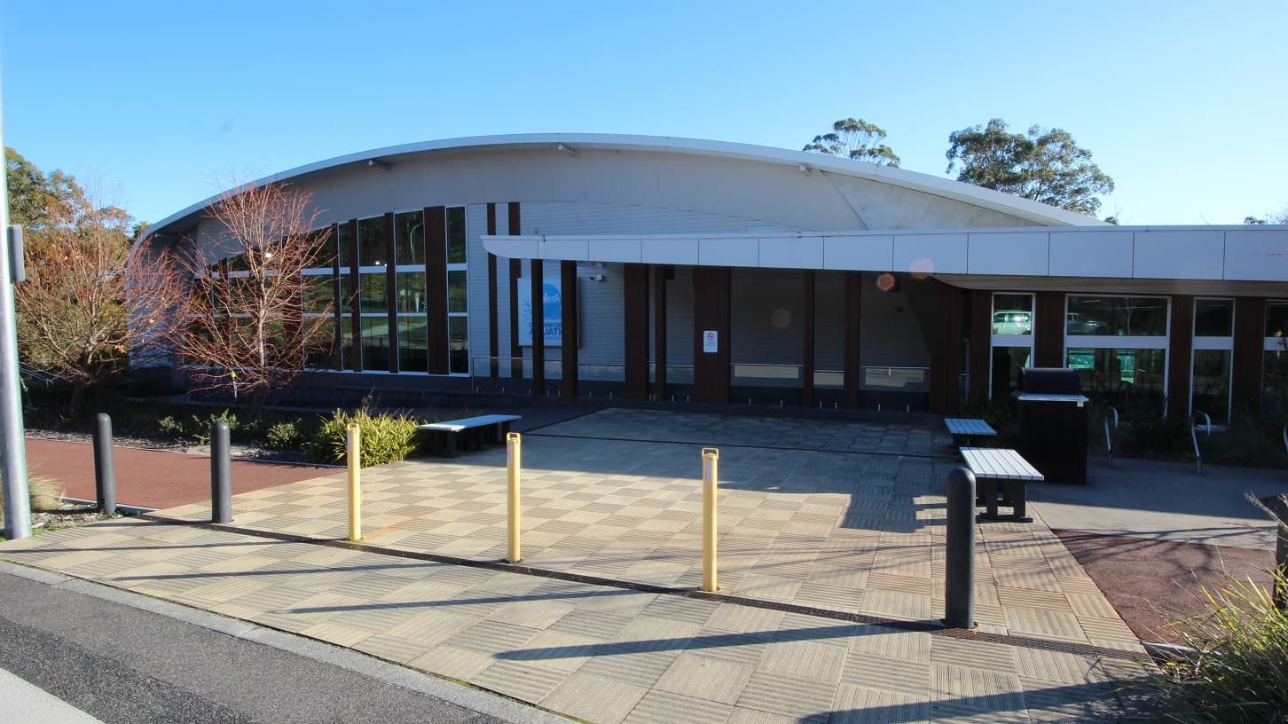 There are designated accessible car spaces located near the entrance of Splash Devonport. These spaces are marked with yellow bollards and yellow lines to indicate that they are reserved for persons with disabilities. Surrounding the car spaces is a pathway to move around the whole venue. On the curbs of the parking area is a plant box with a tree, while others have shrubs with moderate leaf length.