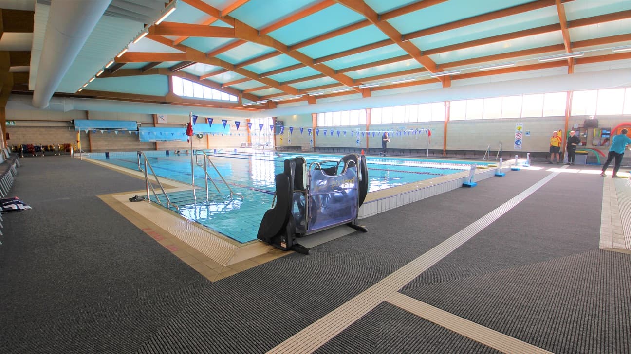 There is a PoolPod accessible hoist in the six-lane, 25-metre indoor pool that starts at 0.9m depth through to 1.8m depth with a 1.2m deep zone. The lanes are separated by red and blue floating ropes. It can be found next to the elevated section at the starting line of the pool and opposite the pool stairs with handrails. Intersecting horizontally to the pool is a string of hanging blue flags tied to opposite poles on the sides of the pool.