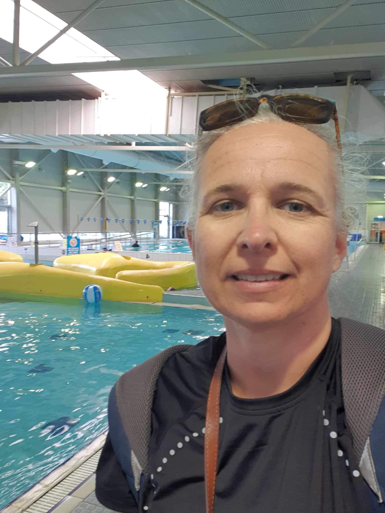 A woman with sunglasses on her head smiles near an indoor pool.