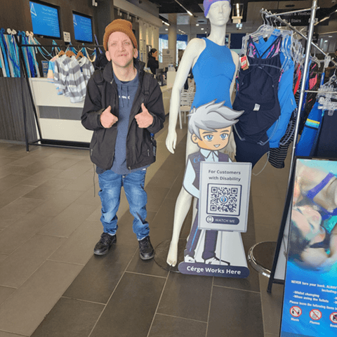 A man in casual wear is posing beside a Cérge cartoon cutout in a store.