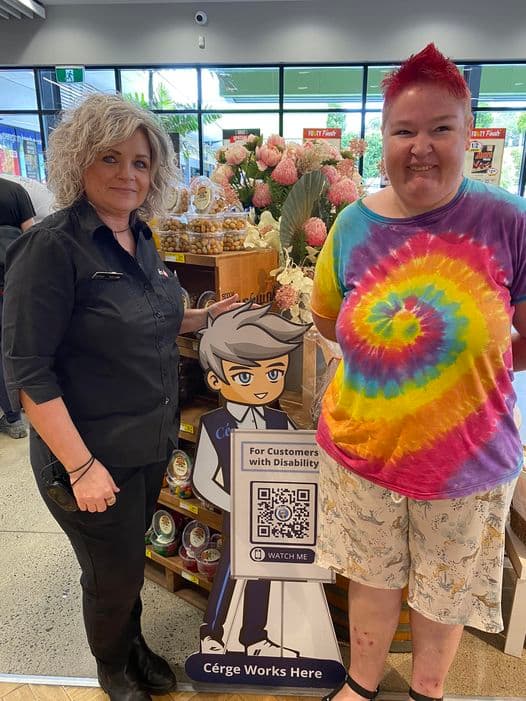A man wearing a mask sits beside a Cérge cardboard cutout with a QR sign.