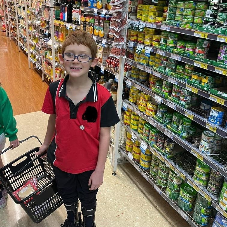 A boy with glasses in a red and black polo shirt is standing in a grocery aisle.