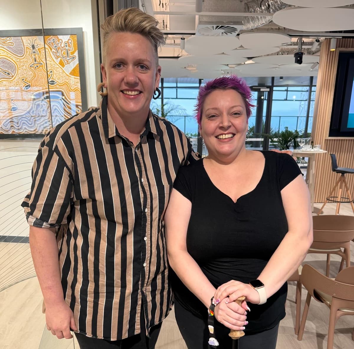 Two people smiling indoors, posing together for a photo.