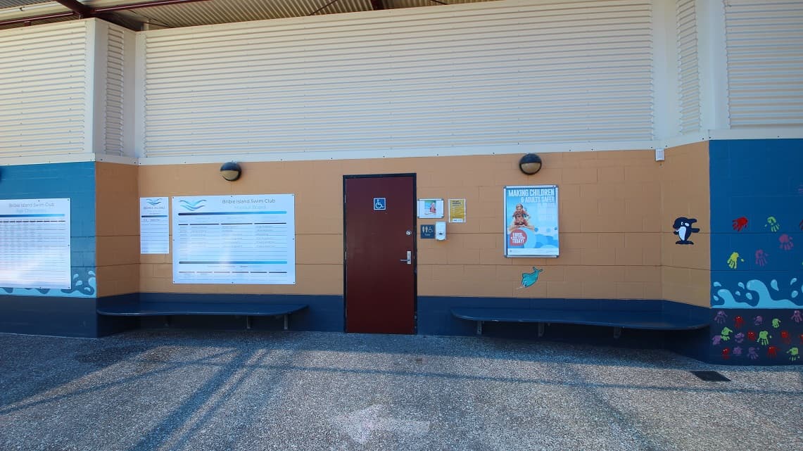 At the entrance, there is a designated area for people with disabilities to enter comfortably. The walls of the building are decorated with various signs and posters that are easy to spot. One specific wooden door has noticeable signage indicating it is for people with disabilities. Additionally, two spacious blue chairs are placed on either side of the main entrance door.
