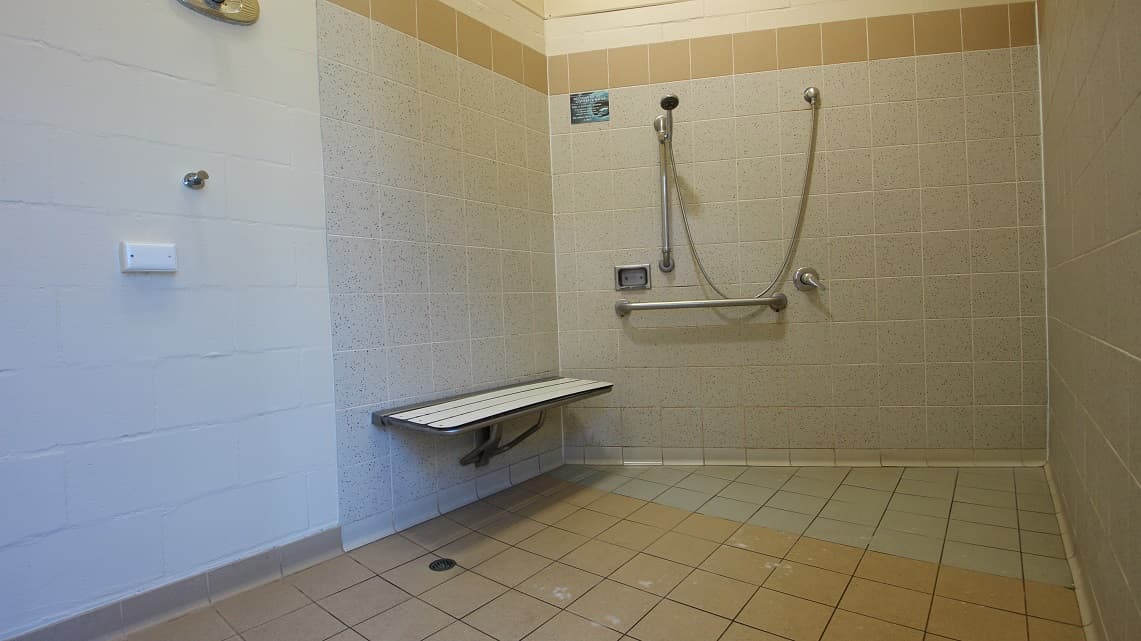 The shower area inside the bathroom of the open-air aquatic area inside Bribie Island. The bathroom is larger than usual for a pool facility. The shower area stands out for its ample space and good upkeep. In the corner near the shower faucet, there is a small metallic chair available for use.