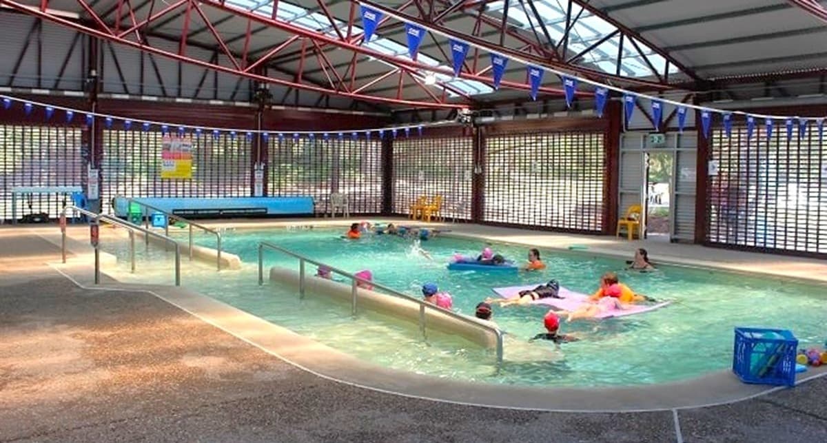 Another angle of the heated pool located inside Bribie Island Aquatic and Leisure Centre. The pool is quite large and can accommodate multiple guests at the same time. There are safety railings are modern and thoughtfully positioned to provide support to the guests. The area is covered with curved, corrugated iron roof lines, adding a unique touch to the overall look of the space.