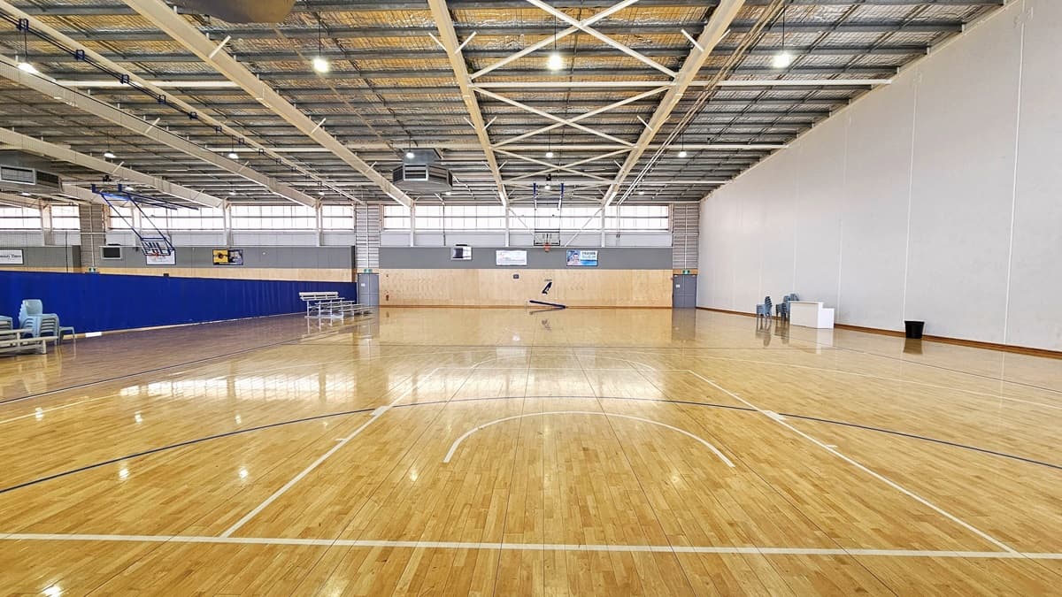 Inside the spacious Court Four. Bench seatings and piled-up chairs are on the left side. Two exit areas located on the left and right side are prominent further ahead. Above the court’s walls ahead, posters are affixed on the gray walls. Next to the white table on the right, there is a black trash bin and chairs.