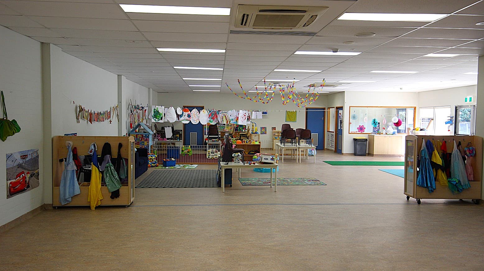 Different costumes for kids are hung in timber-made cabinets. Chairs are arranged carefully at the tables and all toys, drawings, and paintings, are well-organized.