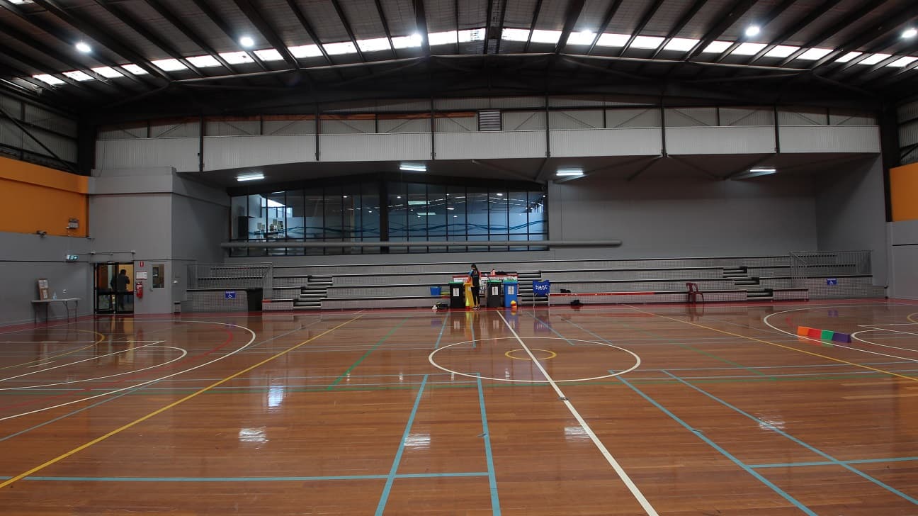 At the side of the two courts is a grey stadium with 4 steps that can accommodate at least 100 people. At the edge of the stadium is a metal railing that separates the audience from the players.