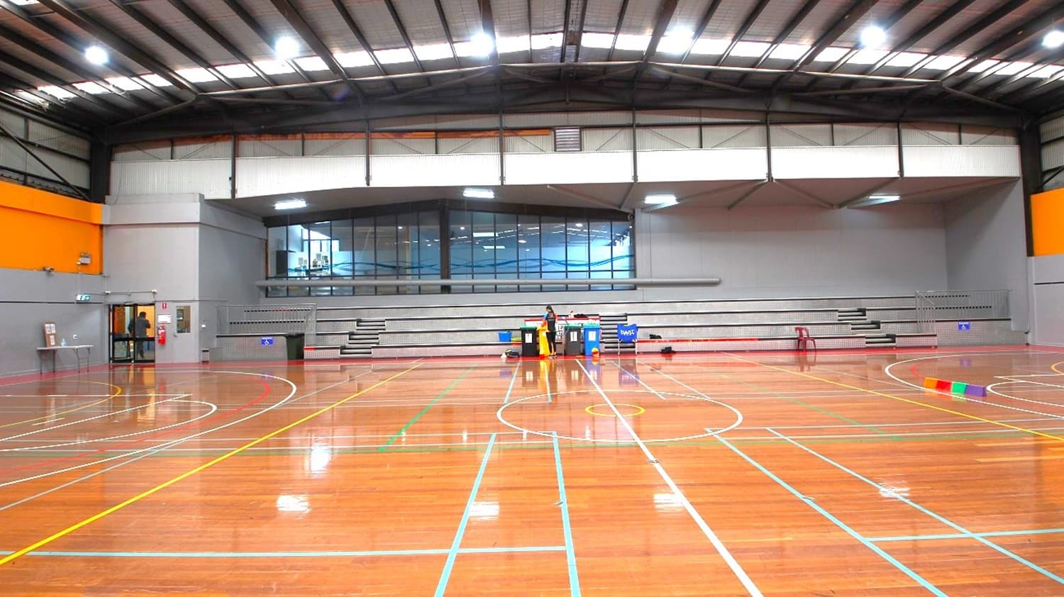 At the side of the two courts is a grey stadium with 4 steps that can accommodate at least 100 people. At the edge of the stadium is a metal railing that separates the audience from the players.