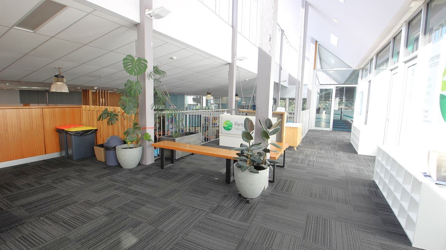 Outside the yoga studio are wood and metal benches, healthy plants, white cabinets, and trash bins. The interior color is white and grey carpet tiles.