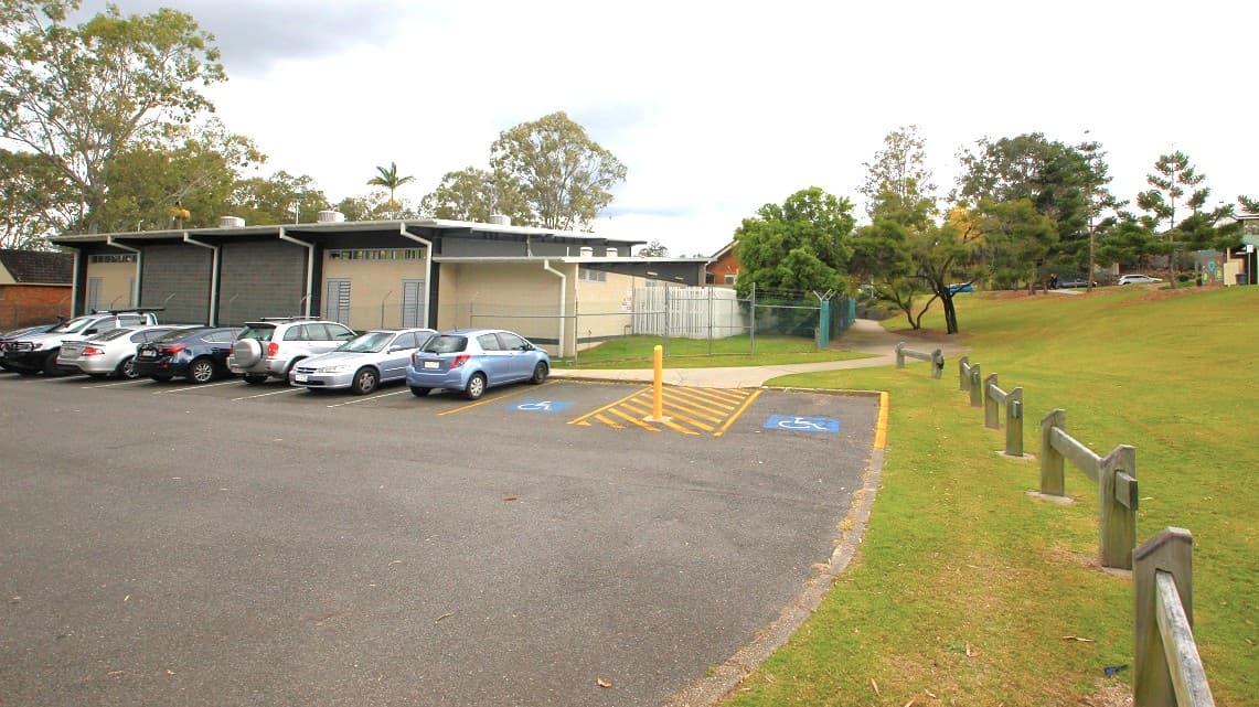 One of the two accessible car spaces. Adjacent to this parking lot, wooden fences have been installed. Sizeable gum trees are also apparent in this vicinity. Metal fences serve as barriers for suburban residences. Designated parking spots are exclusively reserved for individuals with disabilities.