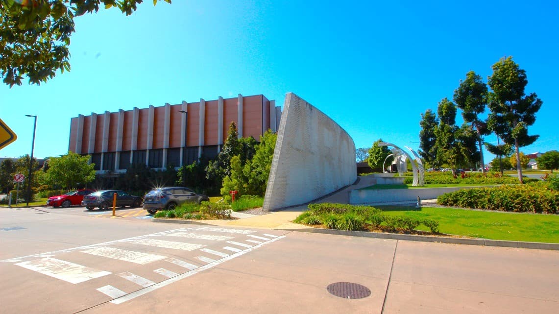Accessible parking area at the Gympie ARC. The Gympie ARC offers a picturesque environment with lush greenery all around. Numerous cars are parked in the vicinity, and the road features prominent road white road marking paint. Also, the exterior design of the Gympie Aquatic Recreation Centre is undeniably contemporary, adding to its overall modern appeal.