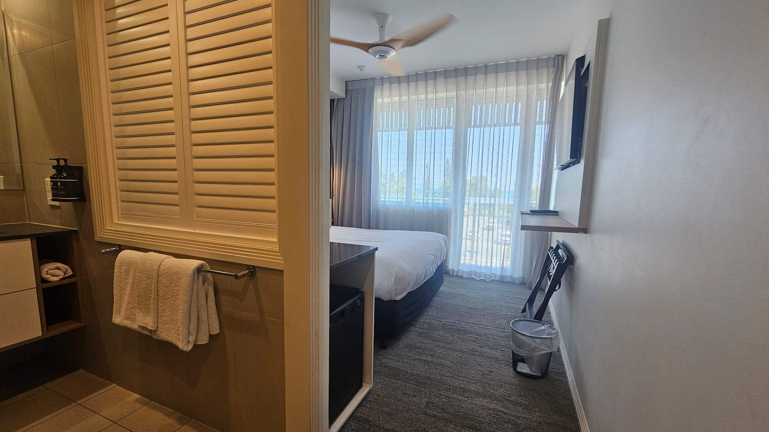 A hallway with two doors, numbered 206 on the left and 207 on the right. The door to room 206 is open, revealing a glimpse of the interior, including a bed, a television mounted on the wall, and a window with sheer curtains. The floor is carpeted in a grey and purple pattern. The ceiling has recessed lighting. Room 207's door is closed and made of wood, with a keycard lock.