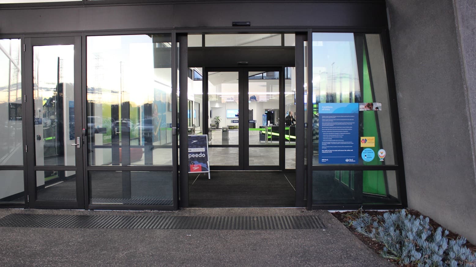 Arrival at Mill Park Leisure, visitors will notice two sets of double doors that are automated for ease of access and a single manual entry door. The doors are made of glass and have black metal edges. On the right side of the manually operating door are the conditions of entry typewritten on blue paper for guests to read and remember while using the venue.