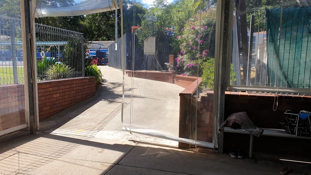At the bottom of the step free ramp to the 25m indoor pool looking back up toward the venue reception. In the image is also the concrete ramp to access the pool, small brown brick retaining walls and plastic walls of the indoor pool.