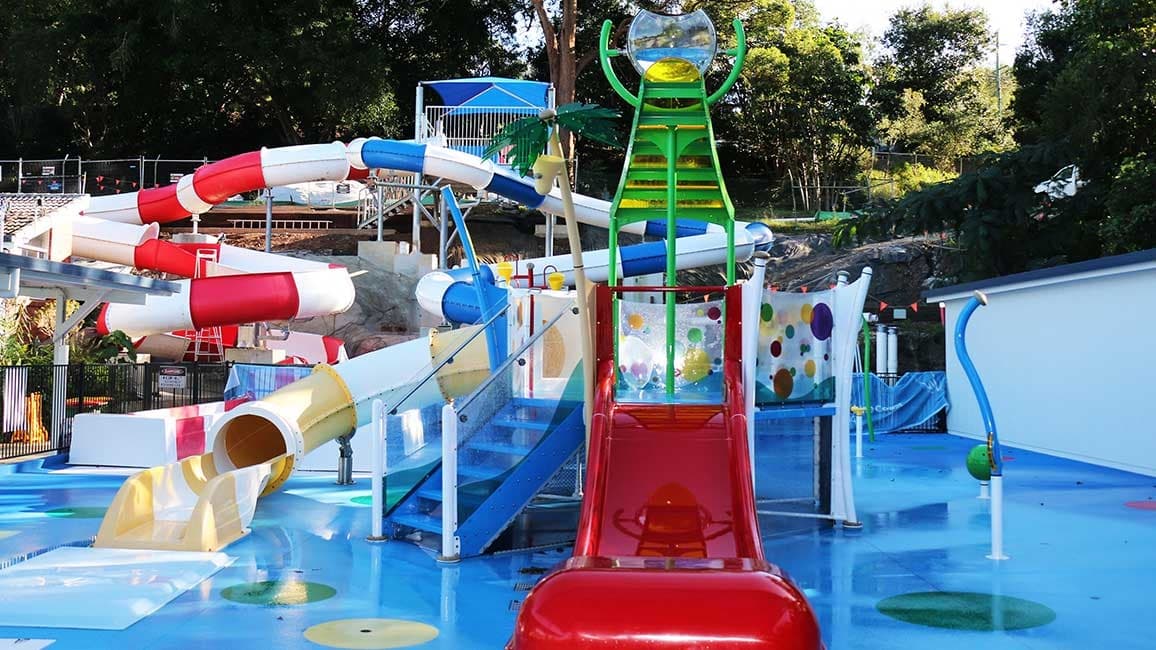 The Nambour Aquatic Centre Splash Park. The aqua blue flooring is contrasted with the red slides and yellow and green equipment.