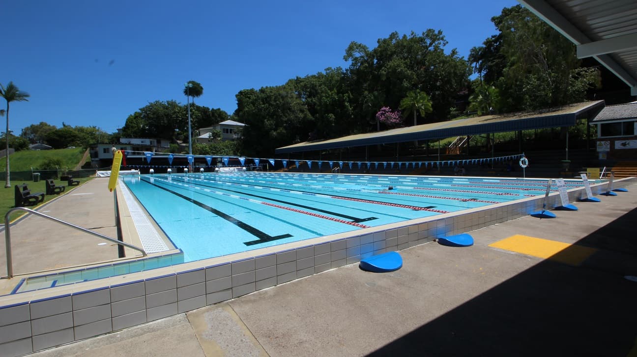 The outdoor 50m pool at the Nambour Aquatic Centre. The pool is 8 lanes wide and set amongst dense green foliage and a spectator stand on the far side of the pool.