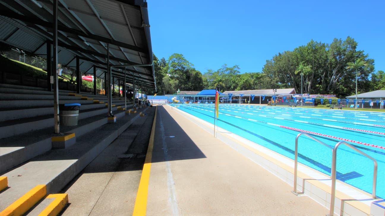 The outdoor 50m pool at the Nambour Aquatic Centre. The pool is 8 lanes wide and set amongst dense green foliage and a spectator stand on the far side of the pool.