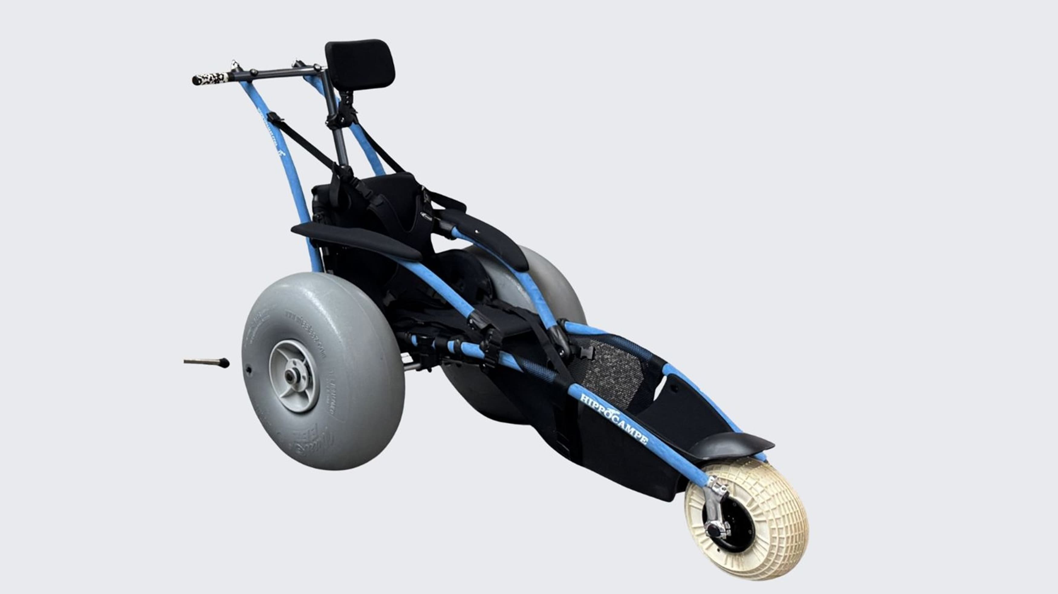A specialised wheelchair designed for outdoor use, featuring a blue frame and large, wide grey tyres for stability on uneven terrain. It has a single front wheel with a textured surface for traction. The seat is black with a headrest, and there are handlebars at the back for pushing. The design is minimalist, focusing on functionality and durability. The background is plain white, highlighting the wheelchair's features.