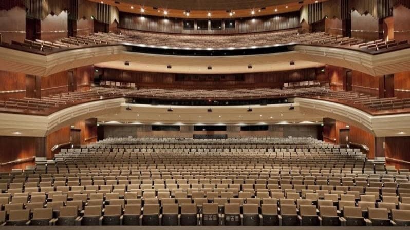 A panoramic view of the concert hall with seating arranged on the first, second, and third levels. The wall features a wooden structure.