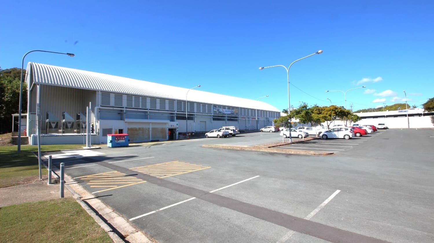 The parking is situated behind the facility and is wide, has plenty of space for cars, tall posts with parking lights, and there is an area with a road sign with yellow slanted lines that indicate no parking is permitted and it is near two bollards.