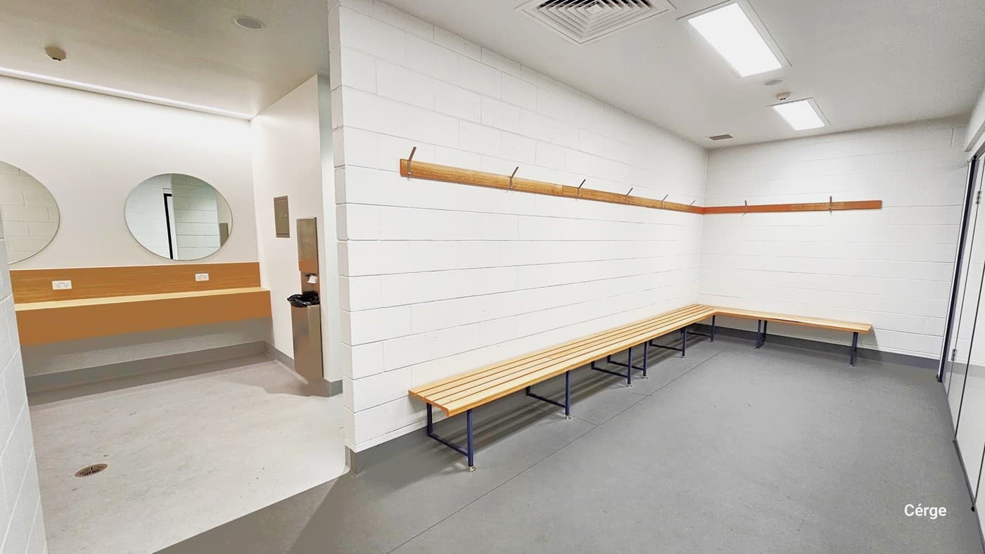 In one of the accessible bathrooms, you'll find an L-shaped wooden bench near the entrance. Above it, a wooden structure is available for hanging items. To the left, there are two round mirrors and a long wooden panel. Adjacent to them is a tissue dispenser and a rubbish bin. The floor has a matte grey and white finish. The ceiling is illuminated by centralized air conditioning and two fluorescent bulbs, ensuring ample light.