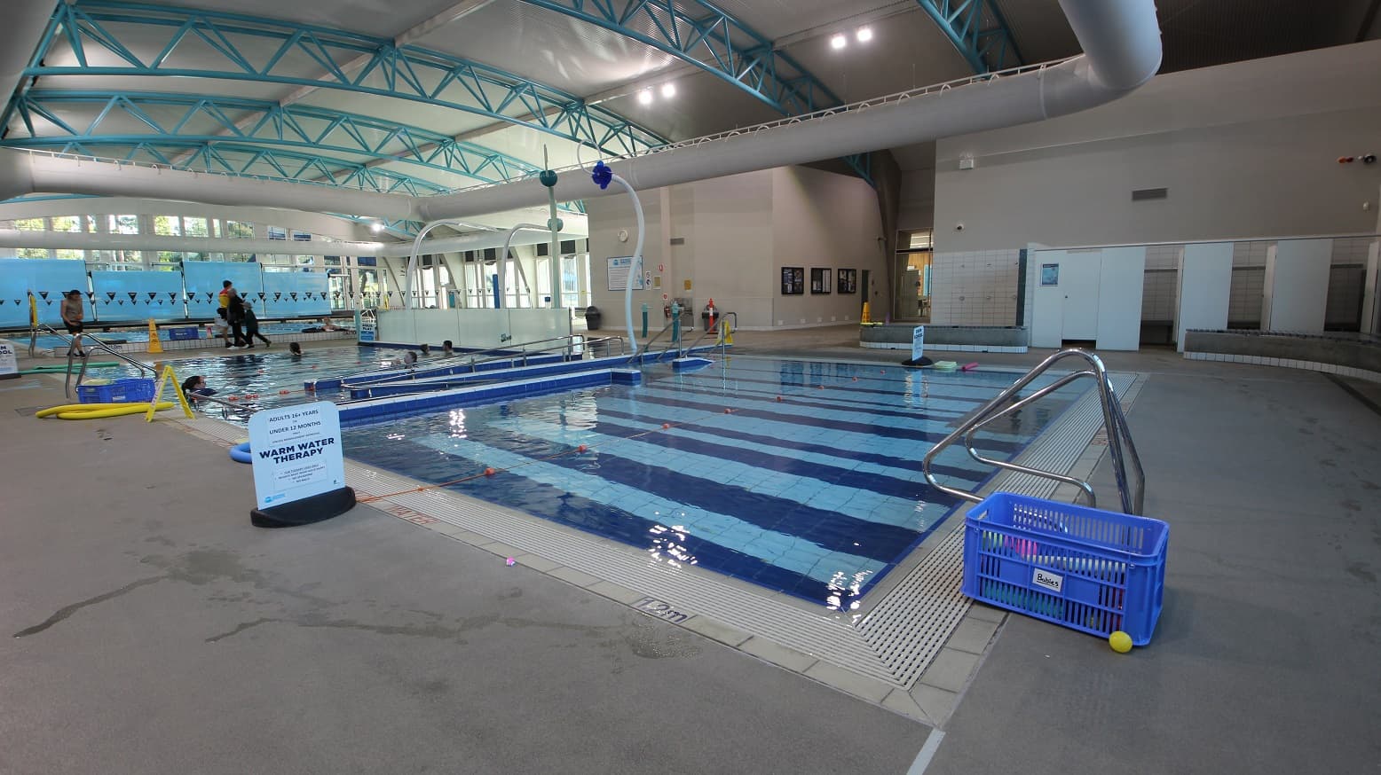 Learn to swim pool plus hydrotherapy or warm water therapy pool. The floor is made of granite floor tiles, and the walls are painted white. At the end of the image are several changing rooms, which can be accessed by turning left upon entering the entrance doors at the venue.