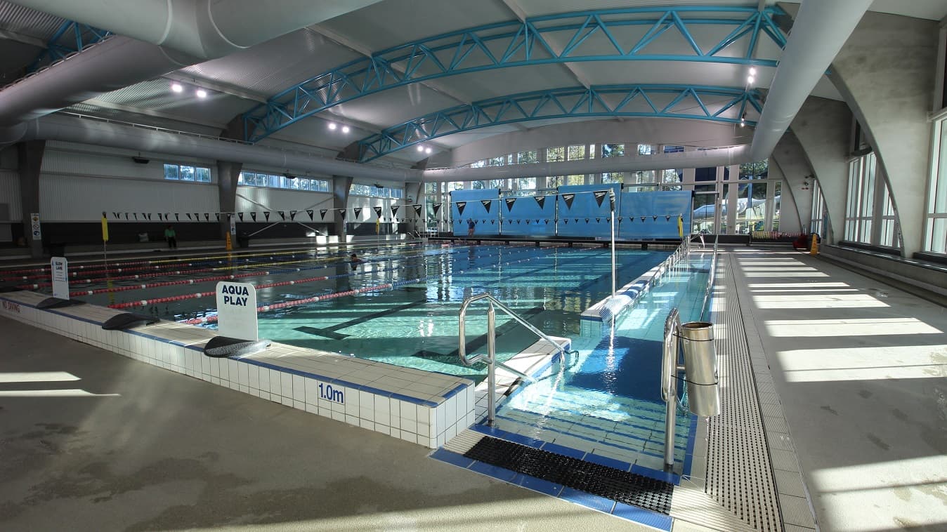 Right side view of the 8-lane 25-meter pool. The entry point to the pool is by the entrance ramp and staircase. On top of the elevated section is the Aqua Play signboard. The pool lanes are separated by red and yellow floating lane ropes, while the others are separated by red and blue lane ropes.