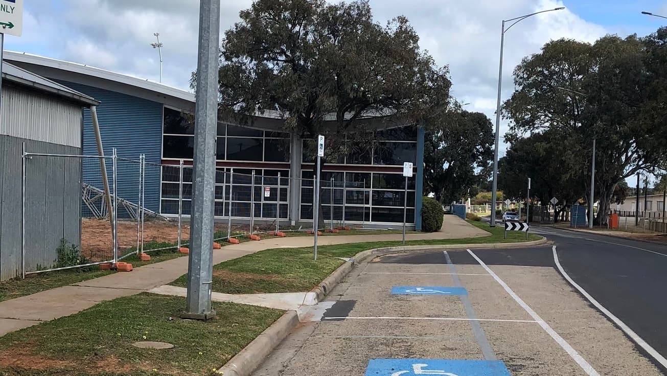 This is the other side of Swan Hill Leisure Centre that’s close to the main road. It has a white pavement leading to the entrance door. There are also several accessible car spaces. From this view, you will see the tall trees and street signs. There is also an unfinished fence being built that has silver line posts without the chain wire.