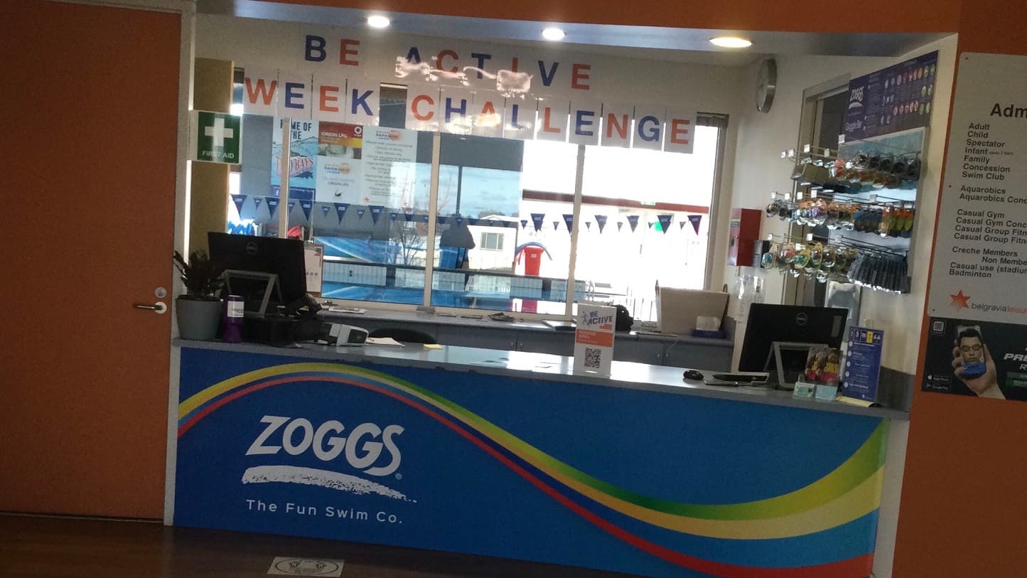This is a closer look of the centre’s main entrance that has a manual glass door with split panels leading you immediately to a retail offering with product display. The right side of the glass door has a glued ad poster saying “Heighten your health & happiness with your first 100 days free”. It has a picture of a lady that wears a red boxing glove. Opposite the glass door is a white wall and to the left is a glass wall that lets you see the green scenery from the outside.