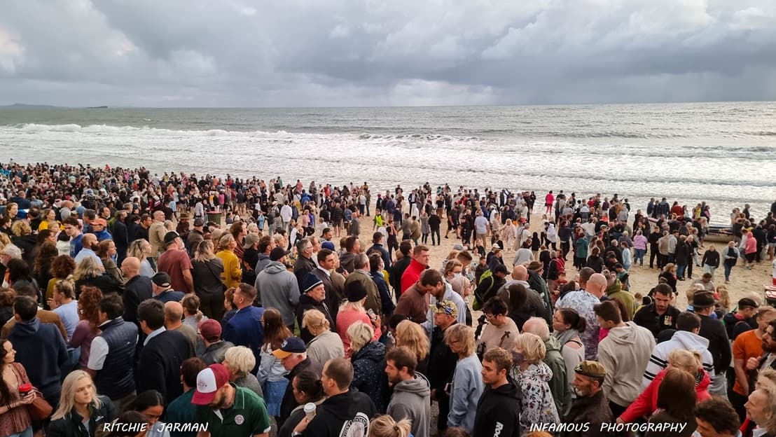 An image showing the ANZAC Day Dawn service with a crowd gathered on the beachfront. The crowd stood on the shore with the sea in the background.