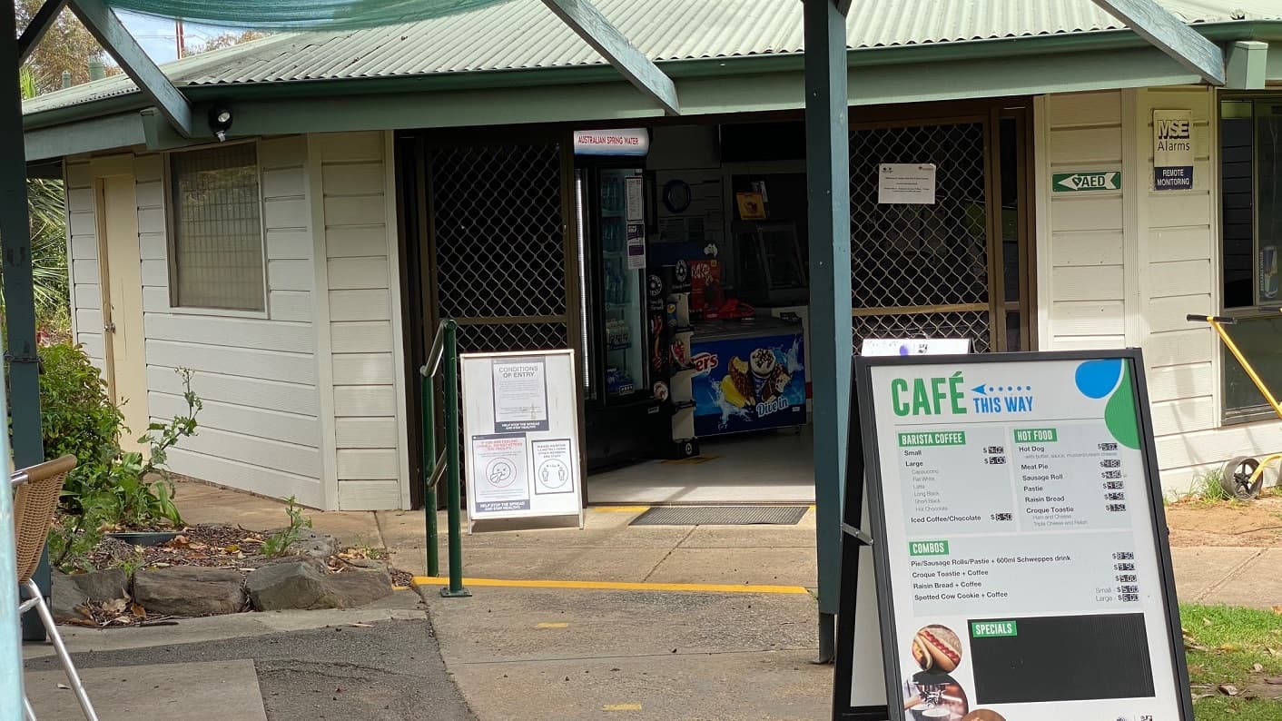 The clubhouse is accessed through a large sliding door, has two notice boards positioned outside and a green handrail is next to the steps. An ice cream freezer is just inside the entrance.
