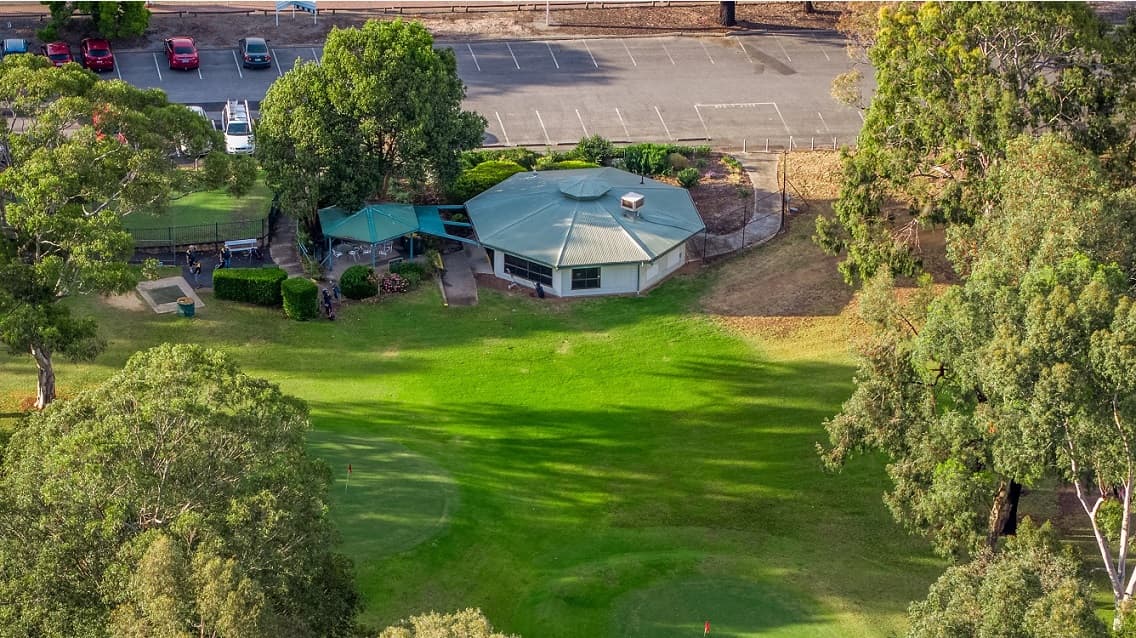An aerial view of the clubhouse, with the car park in the distance and green grass and trees surrounding the clubhouse.