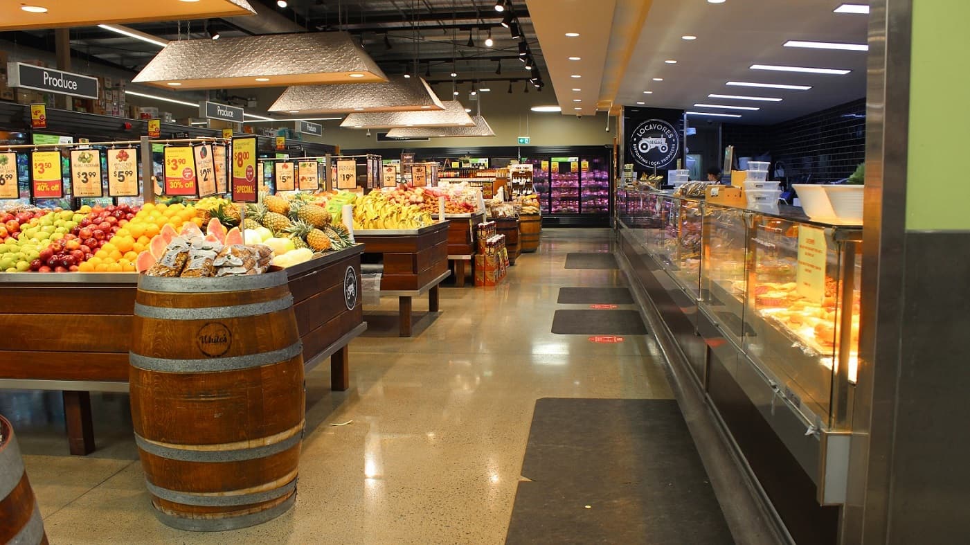 A closer look at the periphery of the hot food section inside White’s IGA Bli Bli. Several black mats are laid on the floor in front of the bread section. Significant lighting is also provided inside by hanging artificial lamps attached to the ceiling of the store.